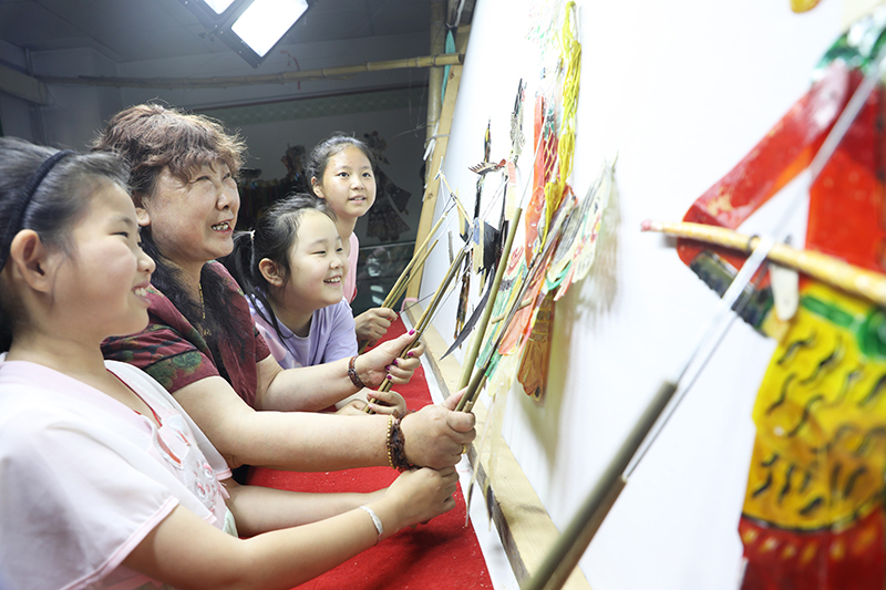 皮影藝人指導(dǎo)小朋友表演皮影戲。